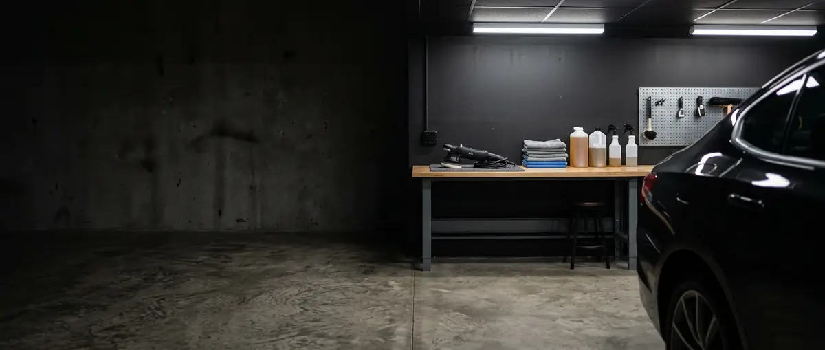 Detailing studio work bench with a dual-action polisher, folded microfiber towels and bottles beside a black car